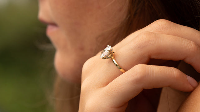 Close up side view of hidden halo lab-grown diamond engagement ring in yellow gold is worn on woman's hand.