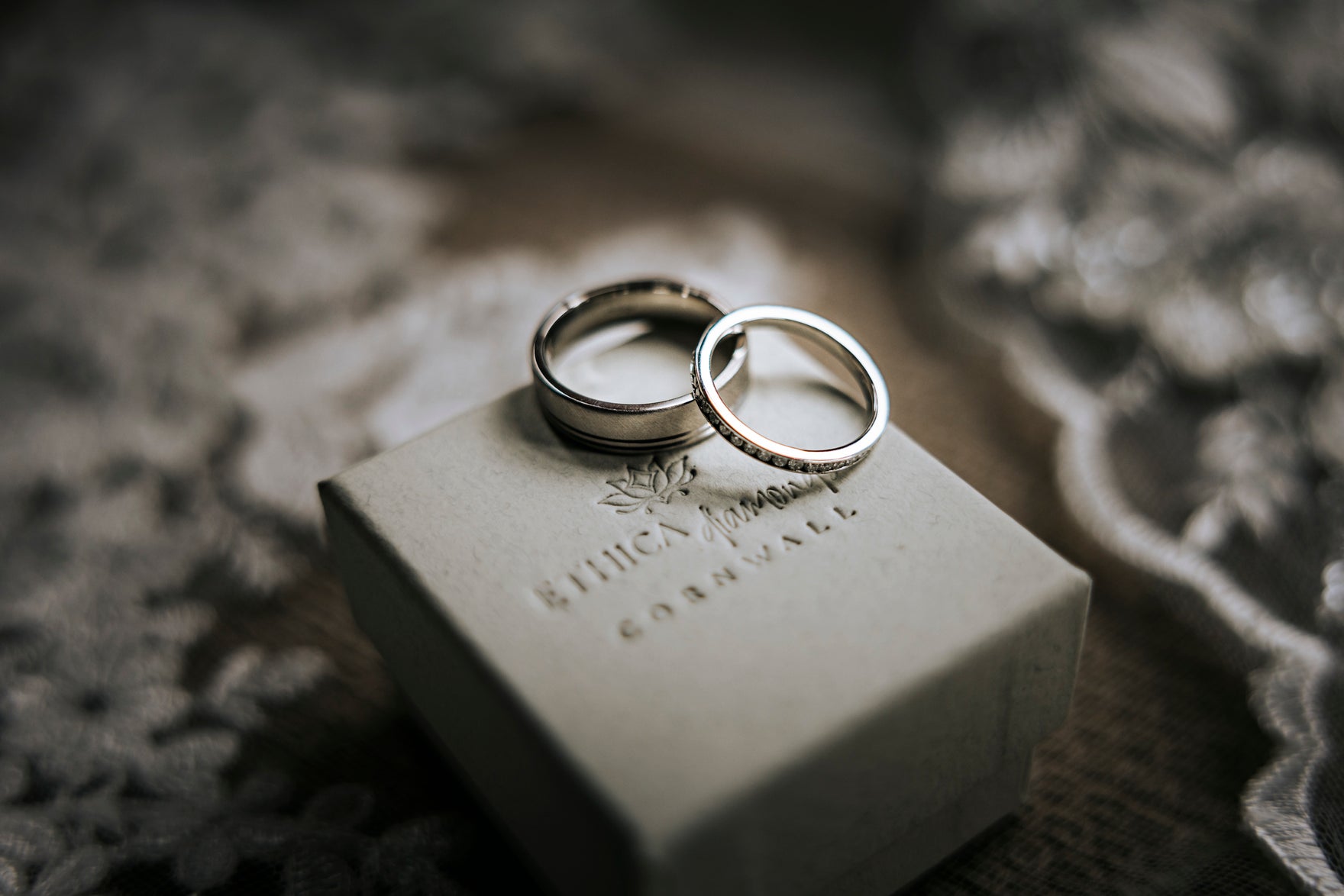 Mr and Mrs wedding rings placed on top of Ethica Diamonds ring box with veil in the background.