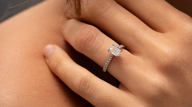 Close up show of classic emerald cut engagement ring with set shoulders worn on woman's hand.