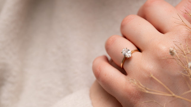 Women wearing a dainty slim oval cut solitaire engagement ring and cream jumper. 