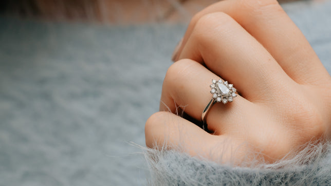 Close up of halo pear cut engagement ring in Platinum, worn on models hand wearing a very fluffy light blue jumper. 