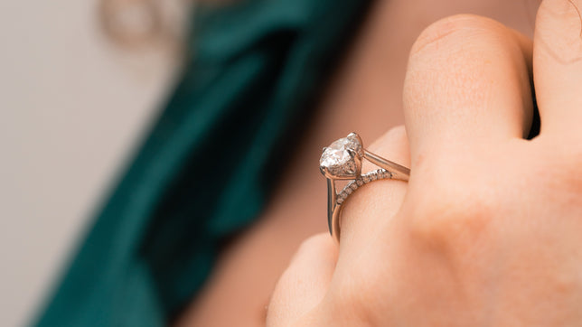 Close up side view of a hidden halo engagement ring set in Platinum with a round brilliant cut centre, worn on the hand of model who's wearing a green shirt. 