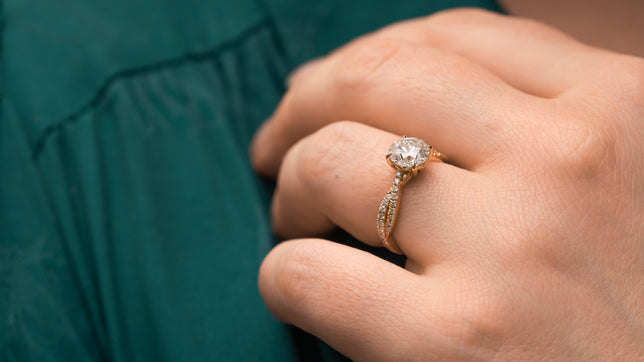 Close up of shoulder set engagement ring in yellow gold with twisted vine design and round centre, worn on model wearing a forest green dress. 
