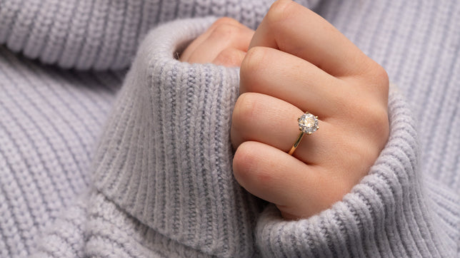 Solitaire lab diamond engagement ring in yellow gold worn on woman's hand wearing a cosy grey jumper. 