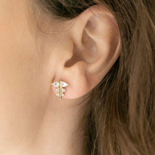 A person models a gold stud earring with diamonds that look like holly
