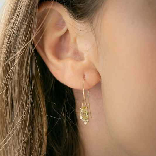 A person models a gold fish hook earring with lemon quartz centrepiece and diamonds.